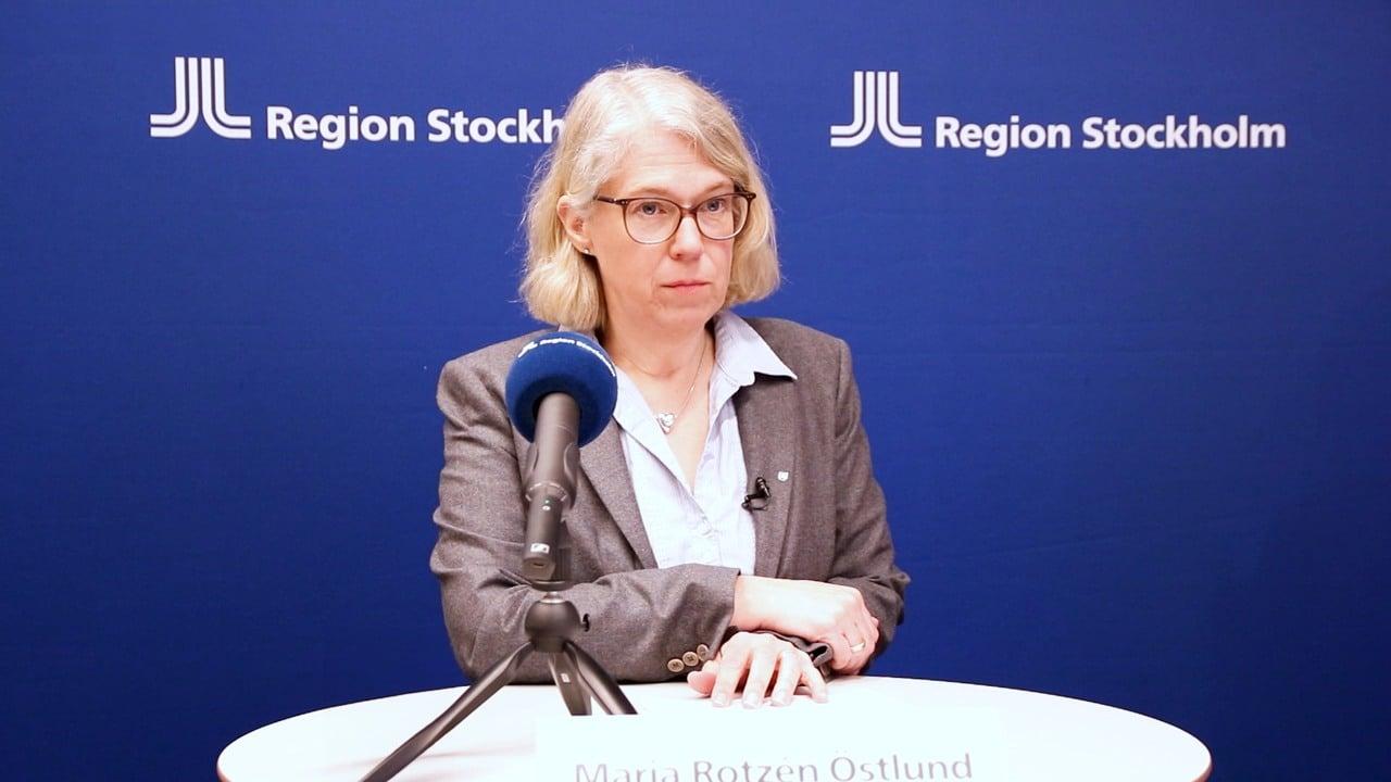 Bild på Maria Rotzen Östlund under en presskonferens. I bakgrunden syns en blå skärm med Region Stockholm logotypen.